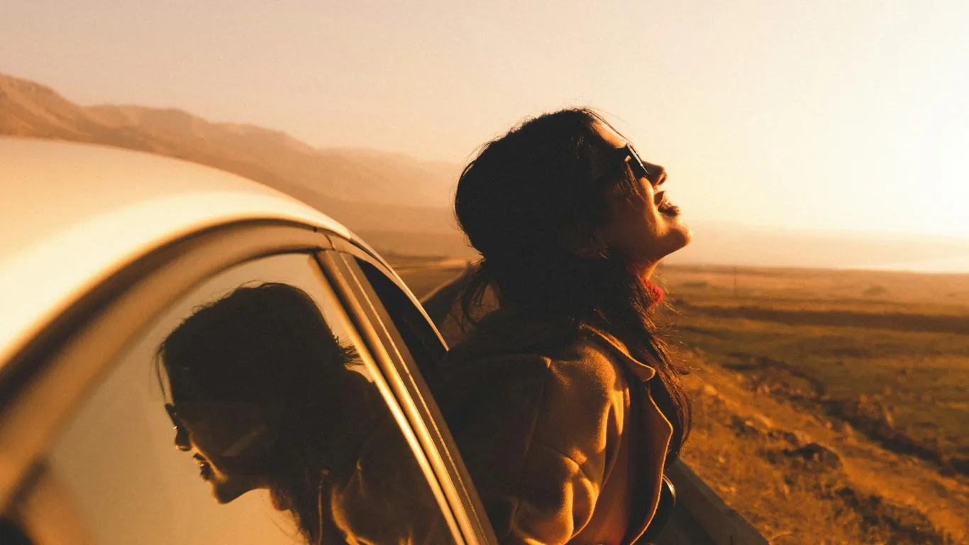 Mujer asomada a la ventanilla de un coche en una carretera al atardecer